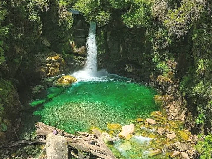 Cascada de aguas claras cayendo sobre una poza entre rocas y vegetación