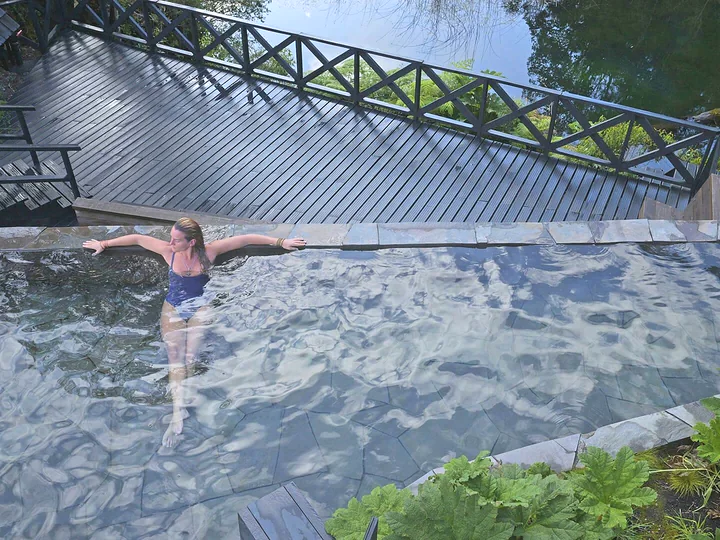Piscina termal y pasarela de madera en un entorno arbolado